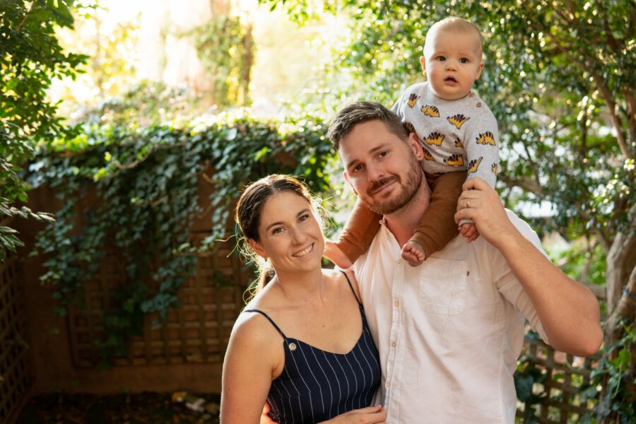 Image of a young couple, man and woman. The man is holding a young child on his shoulders.