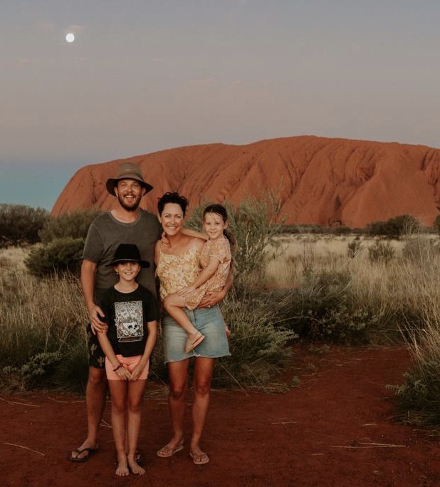 Afbeelding van Lauren met haar man en twee jonge dochters voor Ayres Rock - ook wel Uluru genoemd.