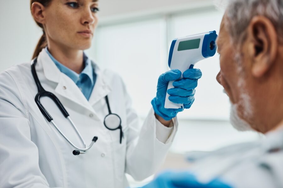Close up of doctor using infrared thermometer while measuring temperature of her senior patient.